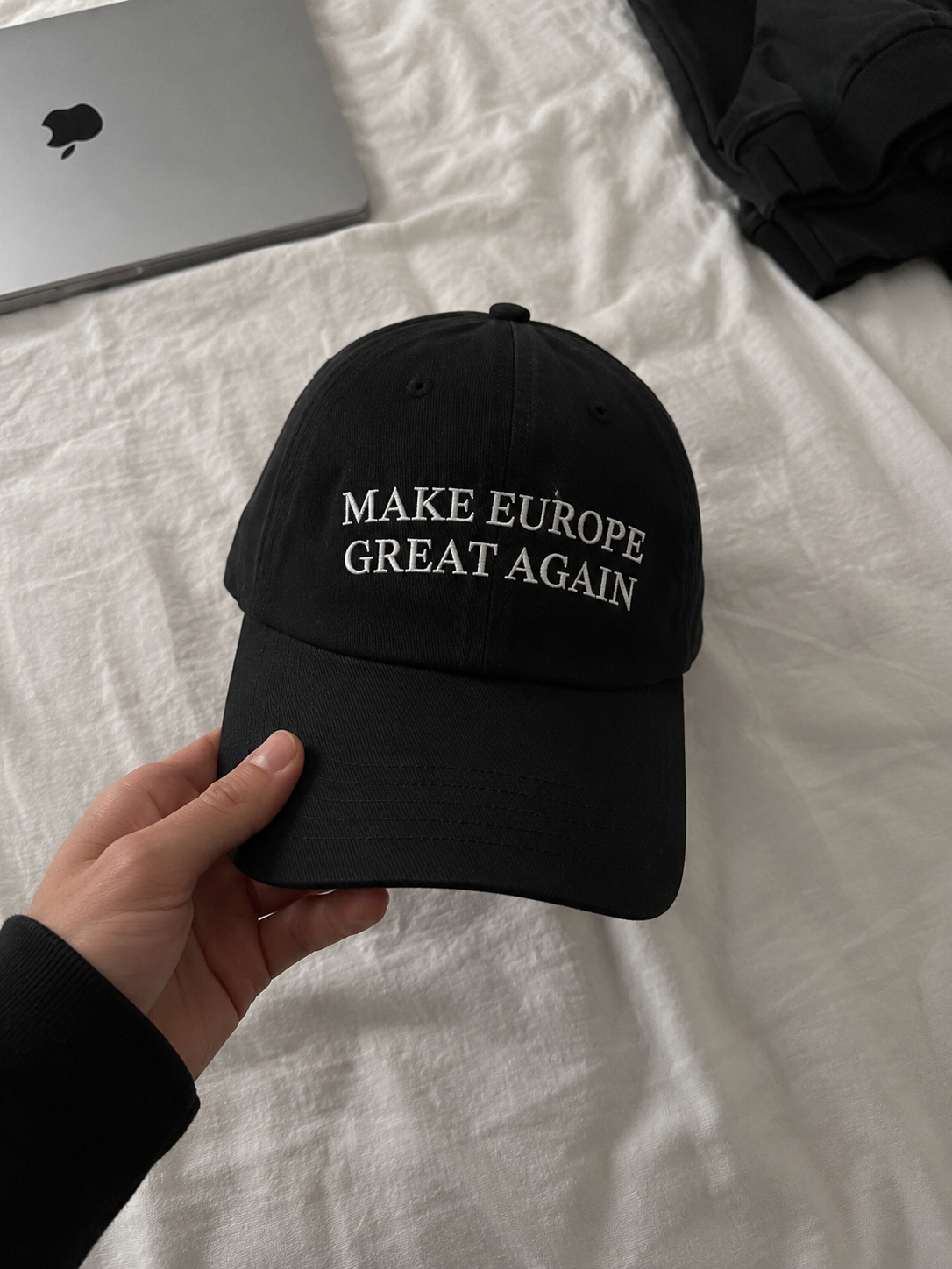 Customer holding the black Make Europe Great Again cap over white bedding