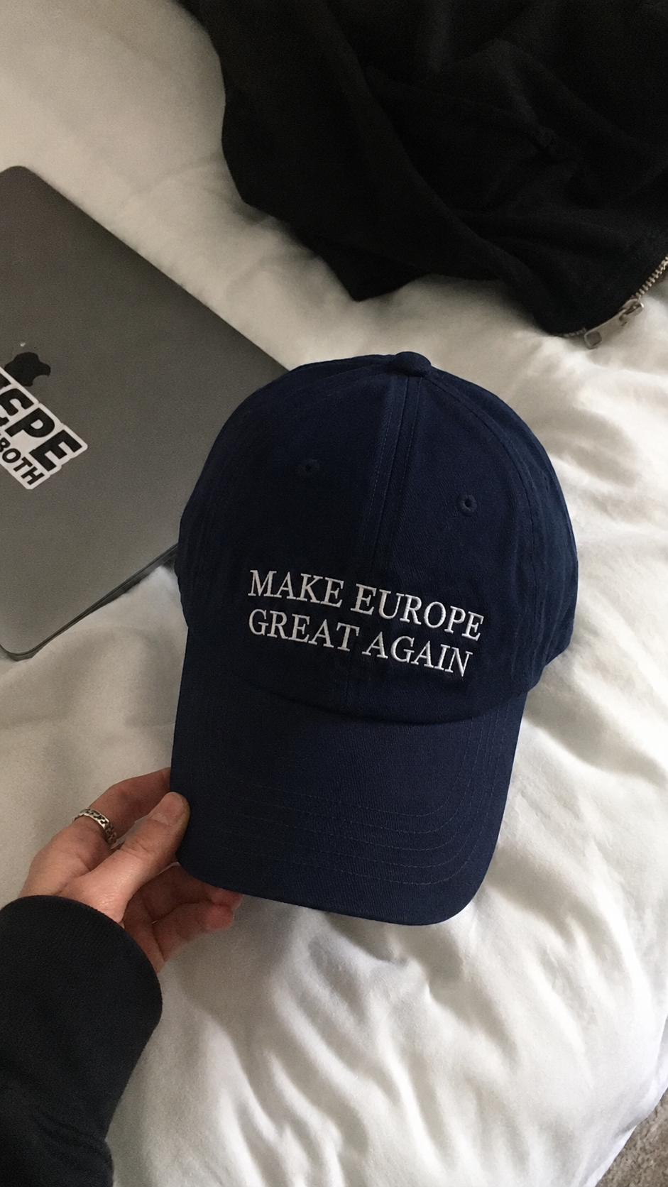 Customer holding the navy Make Europe Great Again cap over a bed